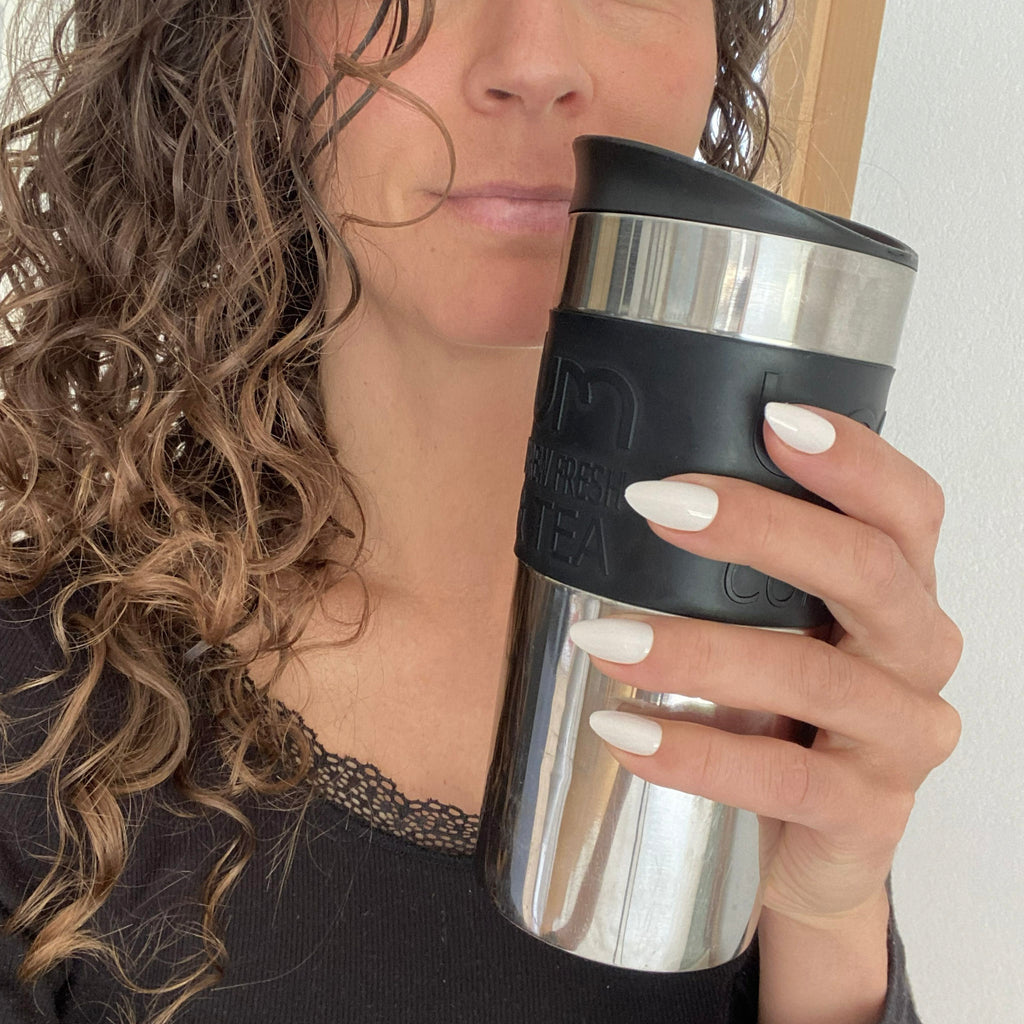Faux ongles Blanc Crème amande courts sur main tenant une thermos à café, cheveux bouclés et tenue casual chic, ongles blanc crème naturel LYLY Nails
