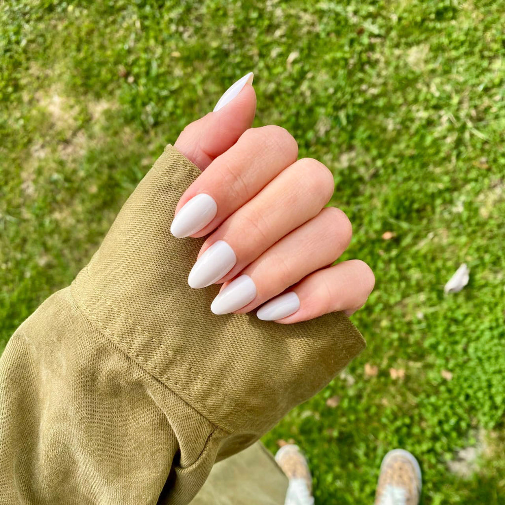 Press-on Nails Blanc Crème forme amande courte portés en extérieur, veste kaki et pelouse verte en fond, manucure épurée et lumineuse LYLY Nails