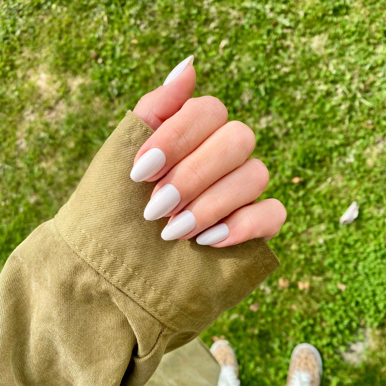 Press-on Nails Blanc Crème forme amande courte portés en extérieur, veste kaki et pelouse verte en fond, manucure épurée et lumineuse LYLY Nails