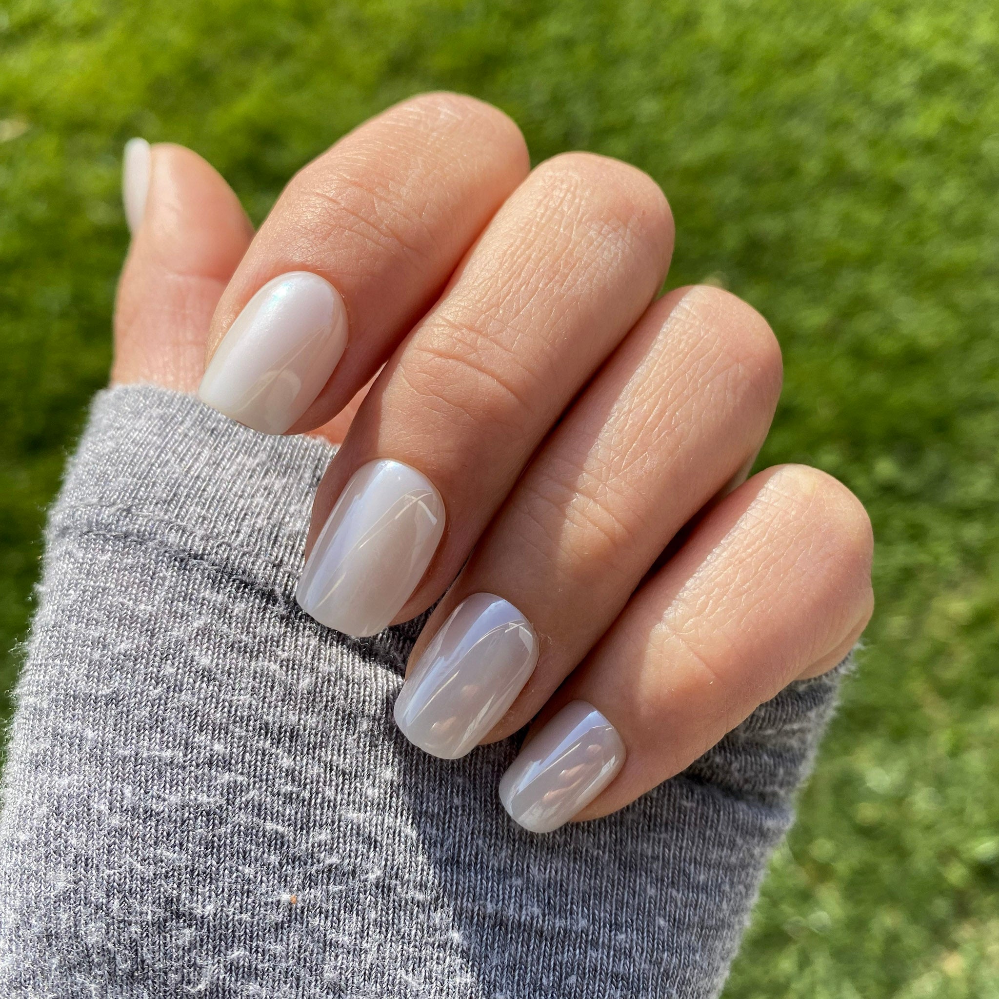 Press-on Nails Blanc Nacré carrés courts portés en extérieur, reflets nacrés sur faux ongles, pull gris et pelouse verte, manucure lumineuse et sophistiquée LYLY Nails