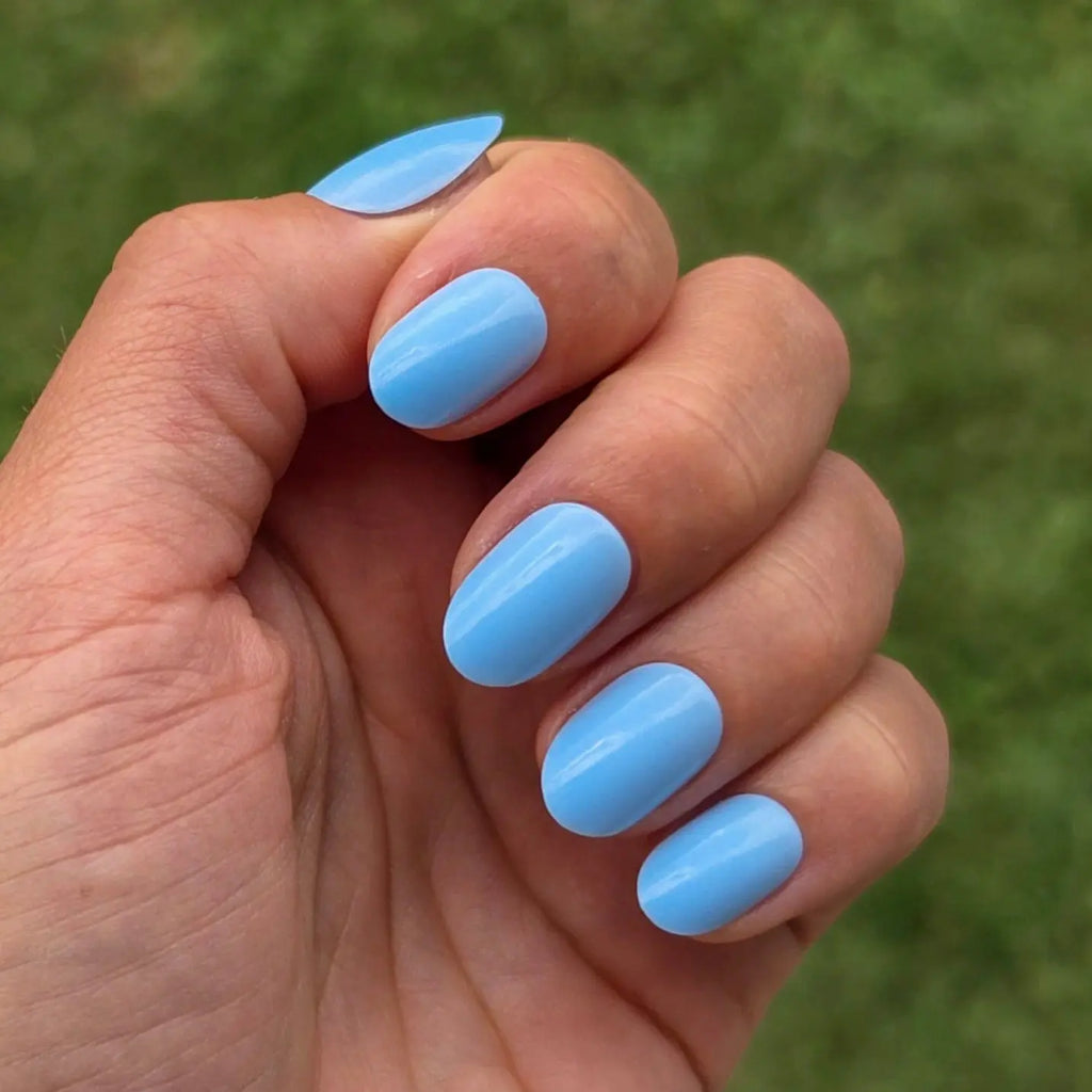 Press-on nails Bleu Ciel arrondi courts poing fermé sur fond de pelouse verte, LYLY Nails