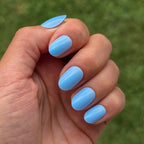 Press-on nails Bleu Ciel arrondi courts poing fermé sur fond de pelouse verte, LYLY Nails