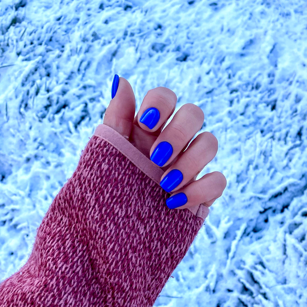 Press-on Nails Bleu Électrique carrés courts portés en hiver, main levée sur fond enneigé, pull rose chiné, ongles faux bleu vif contrastés et audacieux LYLY Nails