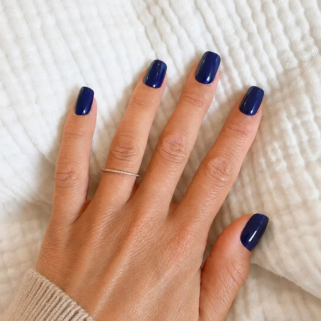 Faux ongles Bleu Nuit carrés courts sur main à plat sur tissu blanc texturé, bague fine dorée et pull beige, manucure bleu marine intense et raffinée LYLY Nails