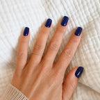 Faux ongles Bleu Nuit carrés courts sur main à plat sur tissu blanc texturé, bague fine dorée et pull beige, manucure bleu marine intense et raffinée LYLY Nails