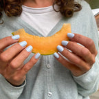 Faux ongles Bleu Perle carrés courts sur deux mains tenant une tranche de melon, gilet gris clair et t-shirt blanc, ambiance estivale fraîche LYLY Nails