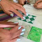 Manucure press-on Bleu Perle carrés courts sur mains en plein atelier créatif, découpage de formes géométriques vertes et blanches, trousses colorées en fond LYLY Nails