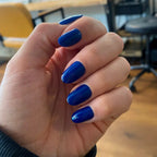 Press-on Nails Bleu Royal arrondis courts sur main au bureau, chaises colorées en fond, faux ongles bleu cobalt vifs et affirmés LYLY Nails