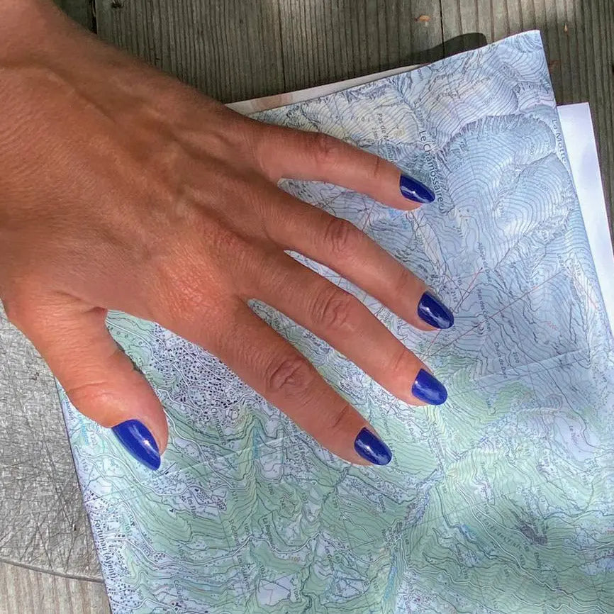 Faux ongles Bleu Royal arrondis courts sur main posée sur une carte de randonnée, ambiance outdoor et aventure, manucure bleue éclatante et dynamique LYLY Nails
