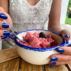 Manucure press-on Bleu Royal arrondis courts, deux mains autour d'un bol de glace framboise en terrasse, haut dentelle blanche, ongles bleus vifs et estivaux LYLY Nails