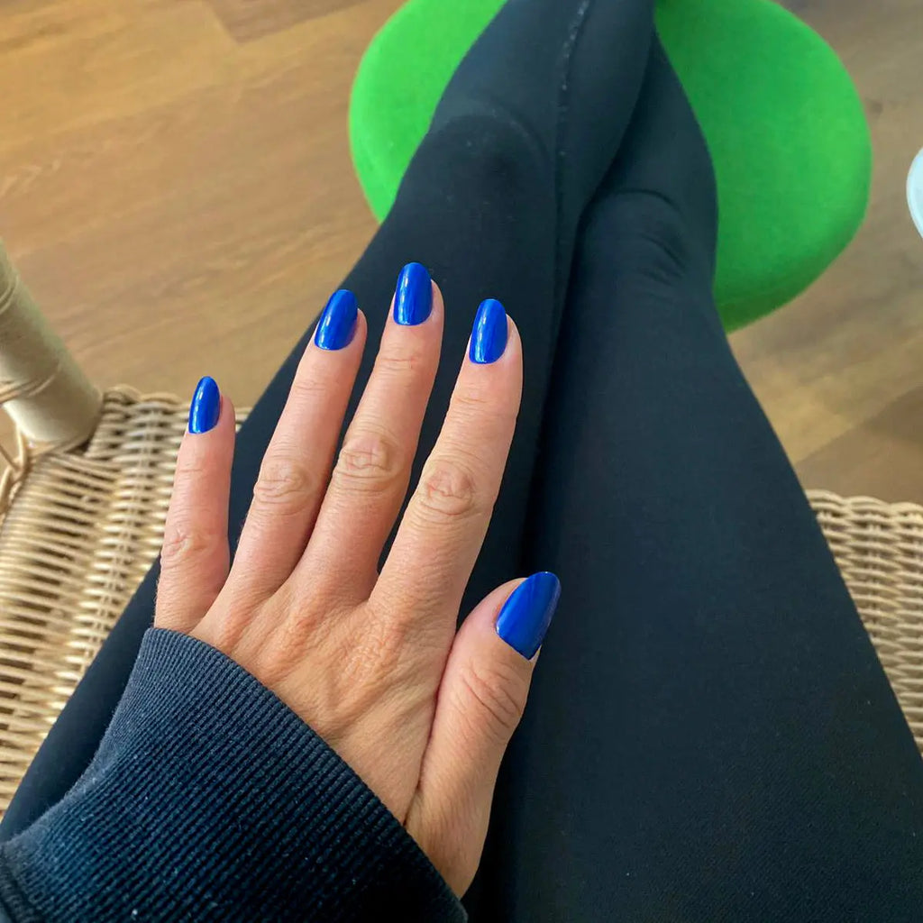 Press-on Nails Bleu Royal arrondis courts sur main posée sur legging noir, tabouret vert et chaise en rotin, look sport chic décontracté LYLY Nails