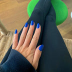 Press-on Nails Bleu Royal arrondis courts sur main posée sur legging noir, tabouret vert et chaise en rotin, look sport chic décontracté LYLY Nails