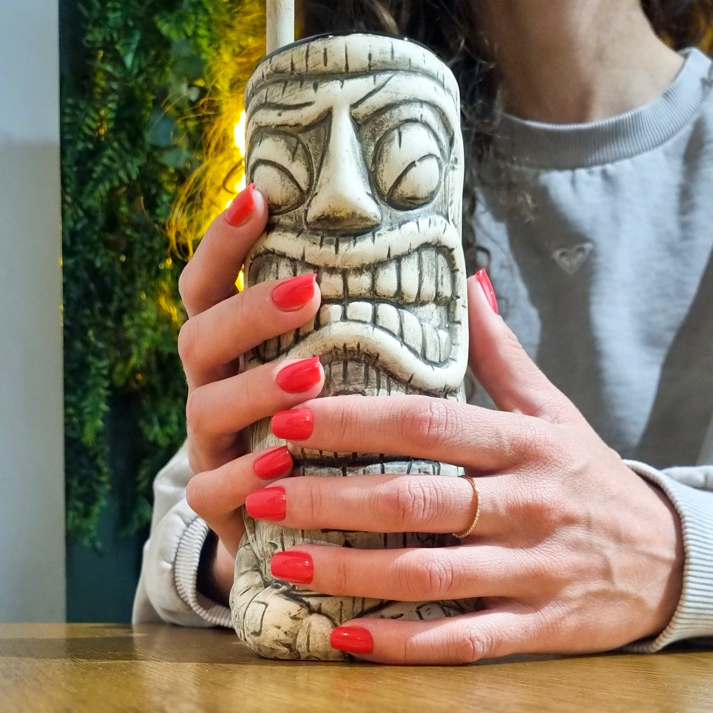 Faux ongles Corail Rosé carré court, deux mains tenant un mug tiki en bar tropical, mur végétal illuminé en fond, ongles rouge corail audacieux LYLY Nails