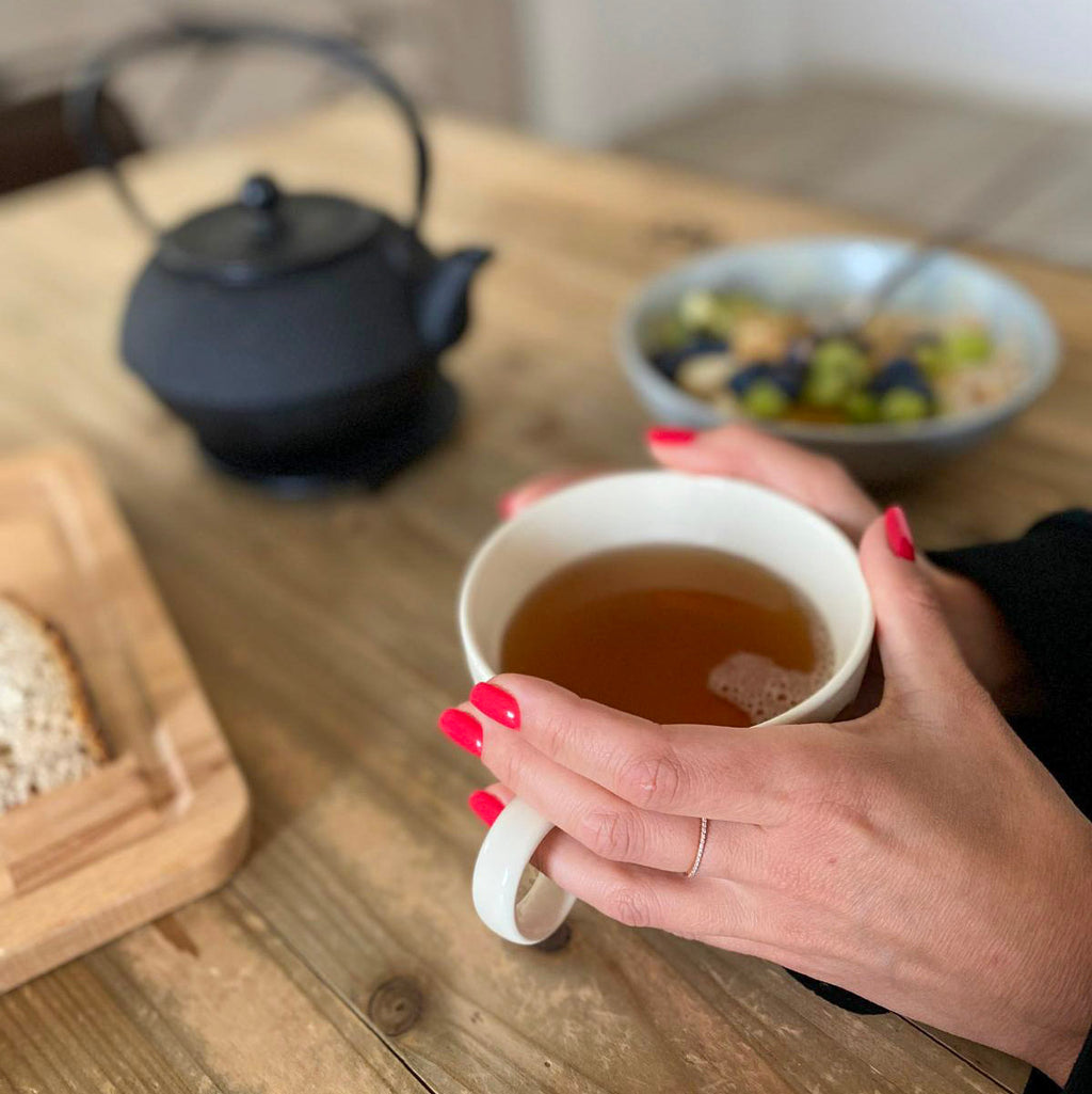 Press-on Nails Corail Rosé carré court, deux mains autour d'une tasse de thé, théière en fonte et petit-déjeuner maison, ongles rouges chaleureux LYLY Nails