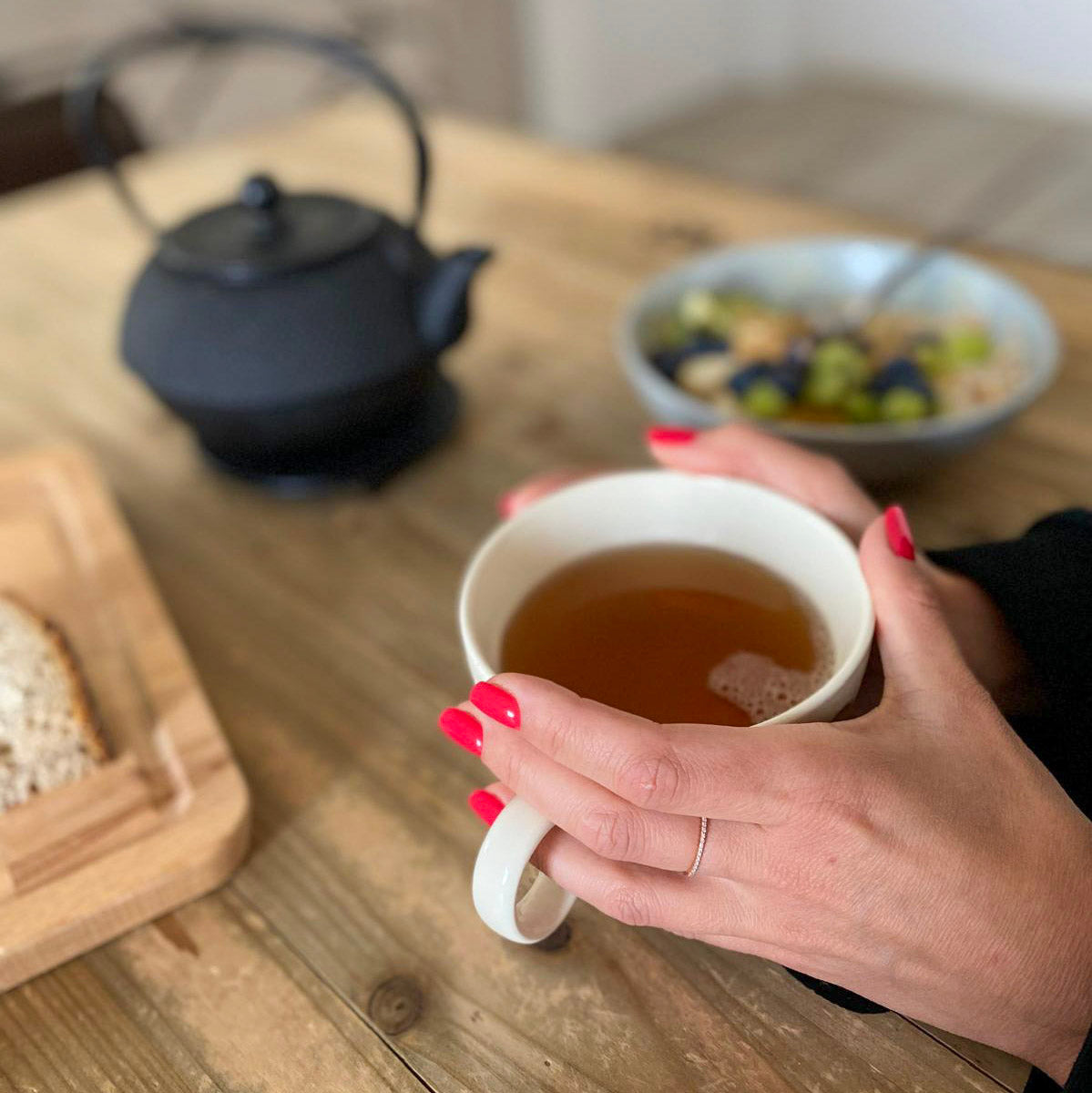 Press-on Nails Corail Rosé carré court, deux mains autour d'une tasse de thé, théière en fonte et petit-déjeuner maison, ongles rouges chaleureux LYLY Nails