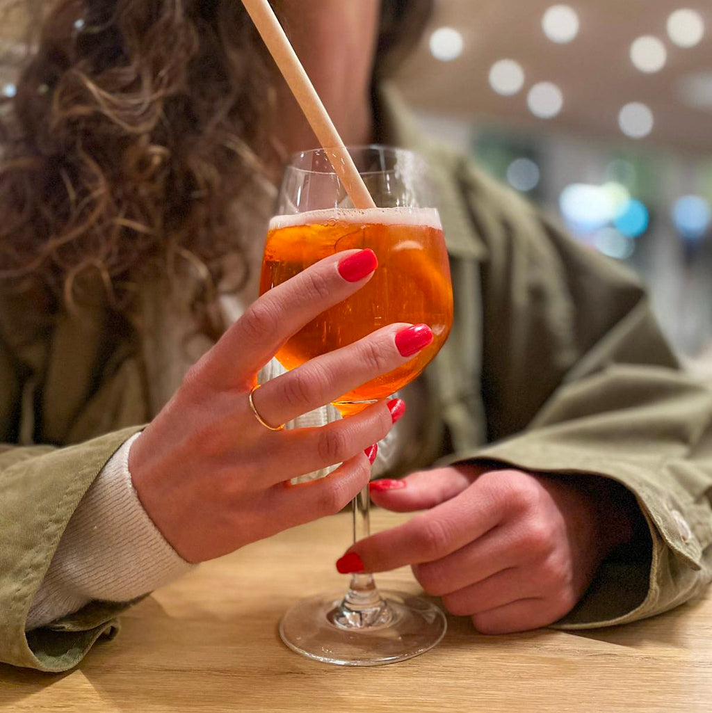Faux ongles Corail Rosé forme carrée courte sur main tenant un cocktail, ambiance bar soirée, ongles faux corail festifs et élégants LYLY Nails
