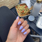 Manucure press-on Lavande Douce amande courte, main devant une pause déjeuner en extérieur, lunch box colorée et gourde, ongles lavande élégants et naturels LYLY Nails