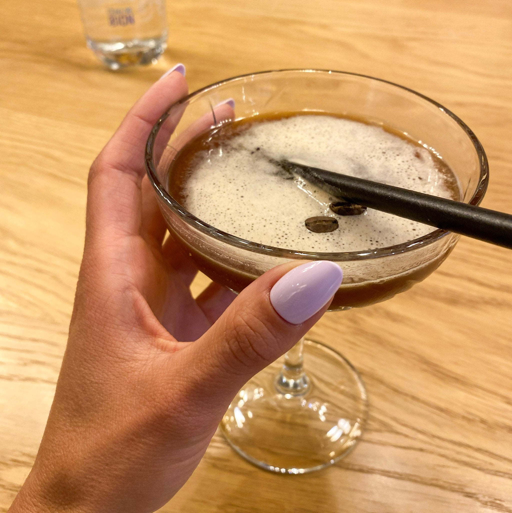 Press-on Nails Lilas Pastel amande courts sur main tenant un espresso martini, ambiance bar tendance, ongles faux violets doux et féminins LYLY Nails