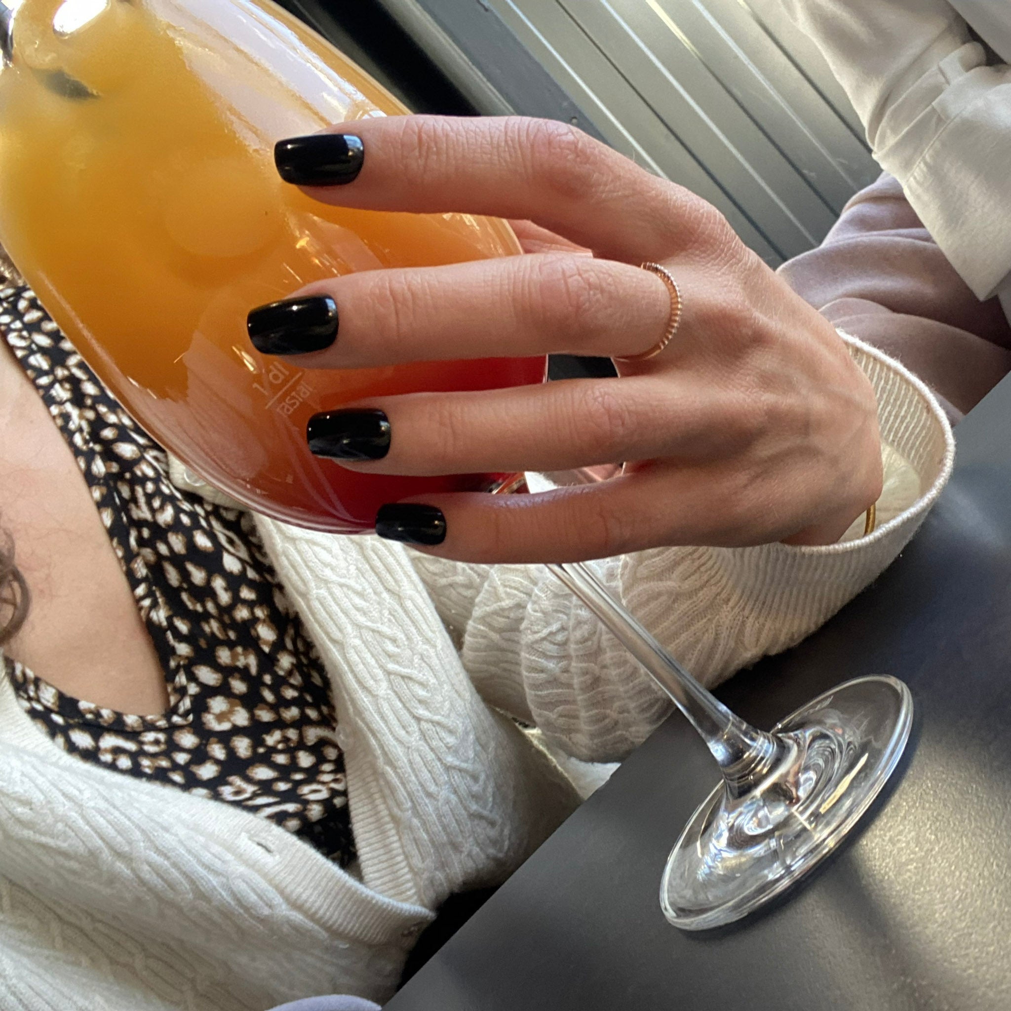 Press-on Nails Noir Intense carrés courts portés au bar, main tenant un cocktail, bague dorée, ambiance soirée élégante LYLY Nails