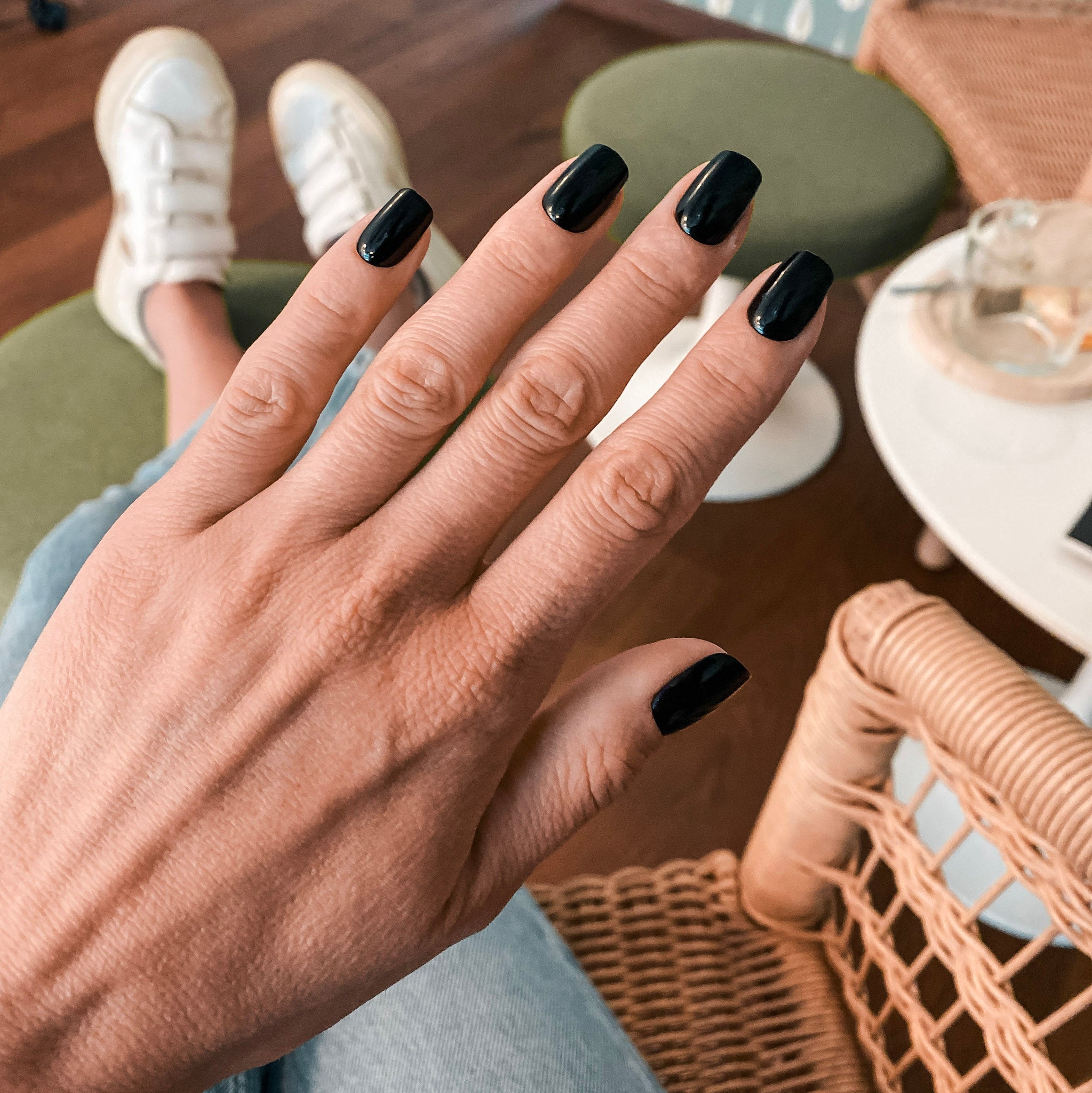 Manucure press-on Noir Intense carrés courts, main ouverte posée en café, ambiance moderne et épurée, ongles faux ultra-soignés LYLY Nails