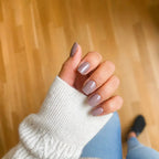 Press-on Nails Nude Cappuccino carrés courts sur main, pull torsadé blanc et jean clair, parquet bois en fond, manucure nude rosé naturelle et élégante LYLY Nails