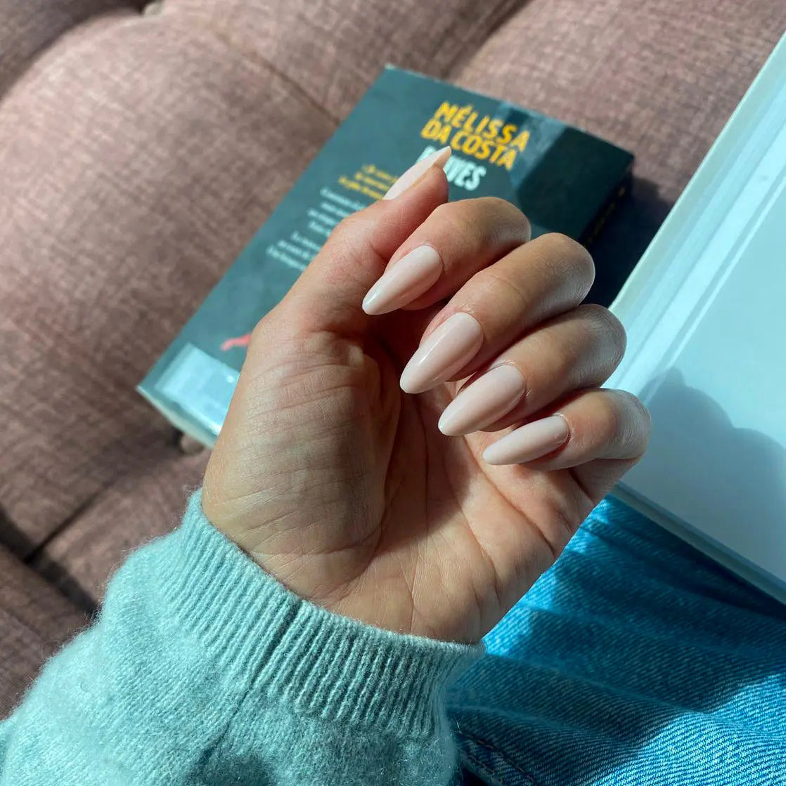 Faux ongles Pêche Douce amande moyen sur main tenant un livre posée sur canapé rose, pull maille bleu mint, ambiance lecture cosy LYLY Nails