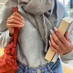 Manucure Press-on Pêche Douce amande moyen sur deux mains en bibliothèque, sac terracotta à franges et livre, gilet et écharpe gris, ambiance cosy automne LYLY Nails