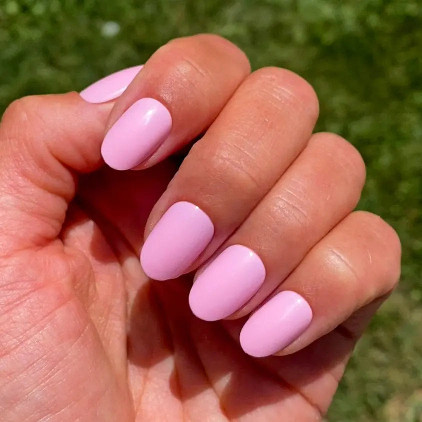 Press-on nails Rose Bonbon arrondi courts main levée sur pelouse ensoleillée, vu de proche, LYLY Nails