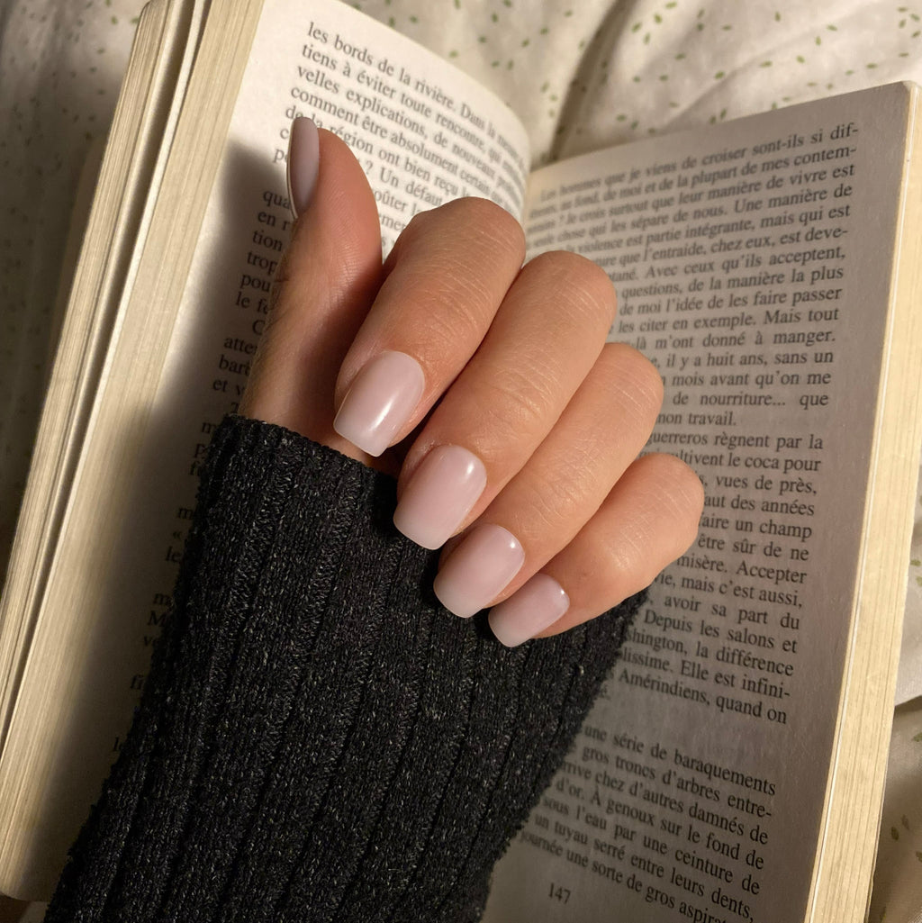 Press-on Nails Rosé Doux carrés courts portés sur main tenant un livre, pull côtelé anthracite, ambiance cosy lecture LYLY Nails