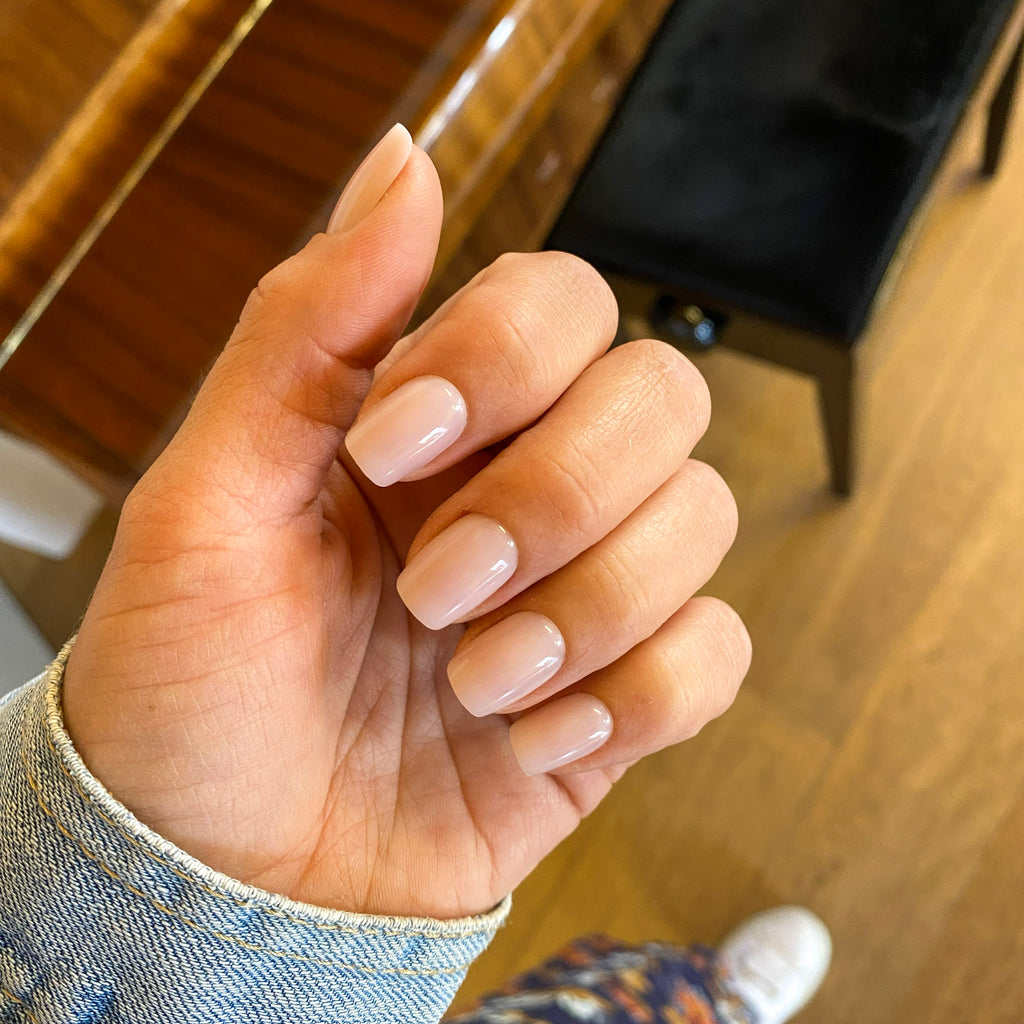 Manucure press-on Rosé Doux forme carrée courte, main naturelle sur fond parquet, veste en jean, ongles faux nude-rosé ultra-soignés LYLY Nails