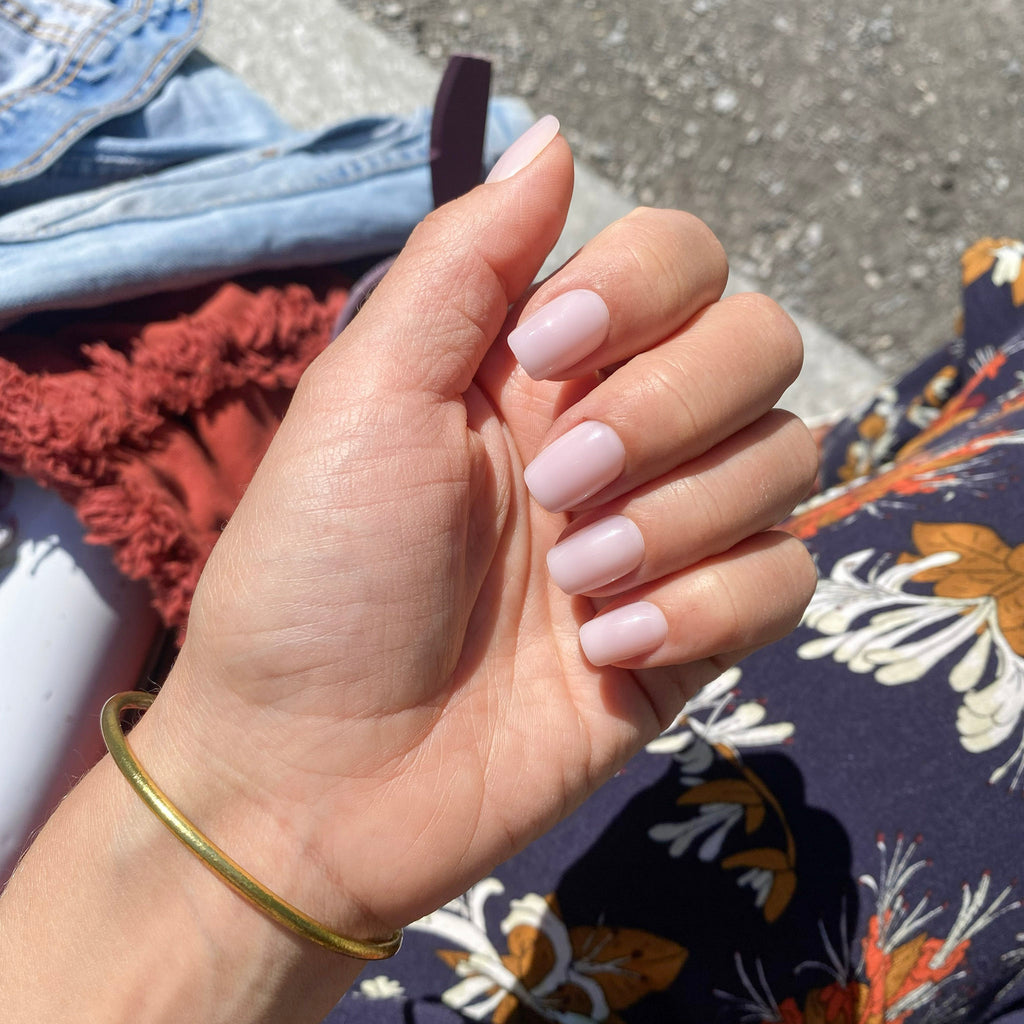 Press-on Nails Rosé Doux carré court portés sur main au soleil, bracelet jonc doré, tissu fleuri coloré en fond, manucure lumineuse et féminine LYLY Nails