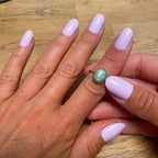 Faux ongles Rose Dragée arrondis courts sur deux mains posées sur parquet bois, bague pierre verte vintage, manucure lilas poudré douce et romantique LYLY Nails