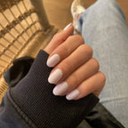 Faux ongles Rose Lait arrondis courts portés sur main posée, pull côtelé noir et chaise en rotin, manucure douce et féminine LYLY Nails