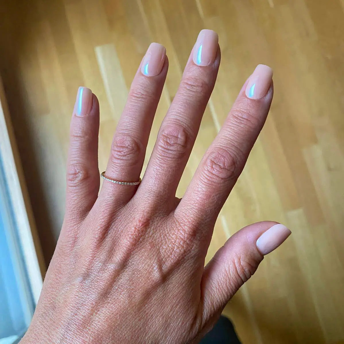 Press-on Nails Rose Nude Brillant carrés courts sur main ouverte, bague fine dorée, parquet bois en fond,faux ongles nude nacré lumineux et naturels LYLY Nails