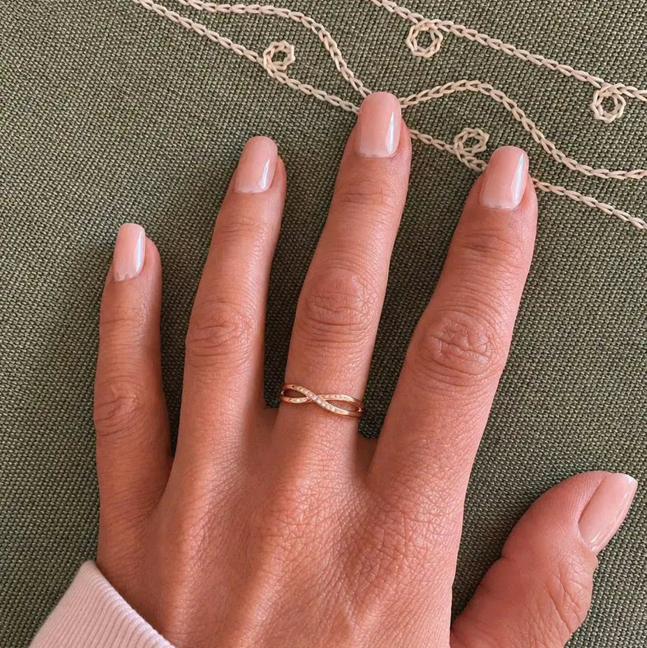 Faux ongles Rose Nude Brillant carrés courts sur main posée sur tissu kaki, bague torsadée dorée et collier en fond, manucure nude élégante et féminine LYLY Nails