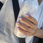Manucure press-on Rose Orchidée amande courte, main tenant une gourde à motifs floraux au soleil, bague dorée, ongles roses irisés et délicats LYLY Nails