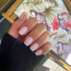 Press-on Nails Rose Poudré carrés courts sur main en poing, pull côtelé noir et tableau fleuri tropical en fond LYLY Nails