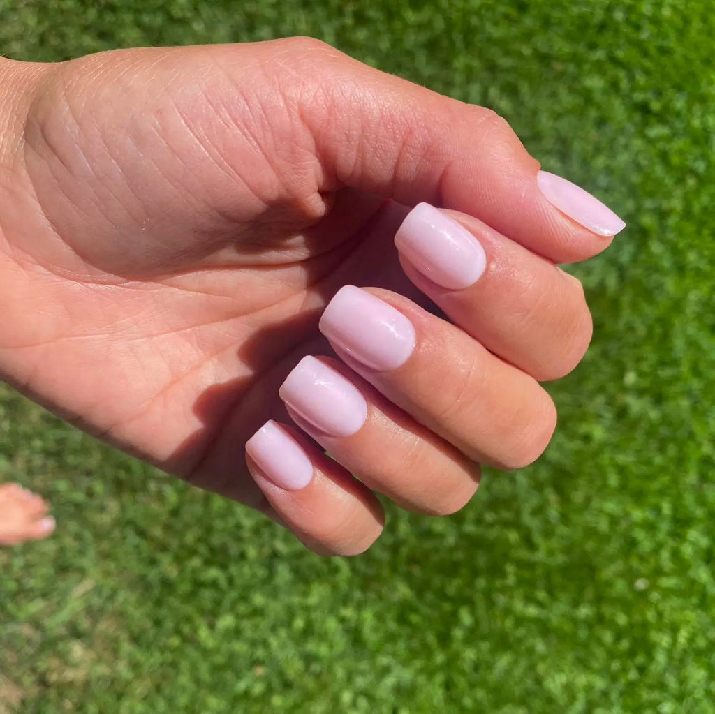 Faux ongles Rose Poudré carrés courts sur main posée sur pelouse verte, lumière naturelle estivale LYLY Nails
