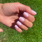 Faux ongles Rose Poudré carrés courts sur main posée sur pelouse verte, lumière naturelle estivale LYLY Nails