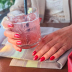 Press-on nails Rouge Tomate arrondi courts deux mains tenant un verre en terrasse de restaurant, LYLY Nails