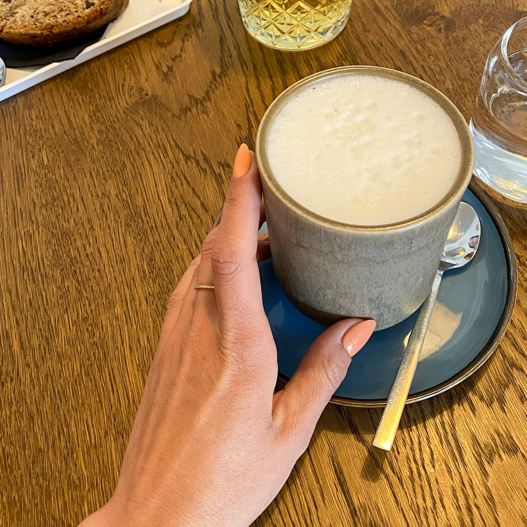 Press-on Nails Summer Spritz arrondis courts sur main tenant un latte en café, tasse céramique et table bois, faux ongles orange pêche doux et féminins LYLY Nails