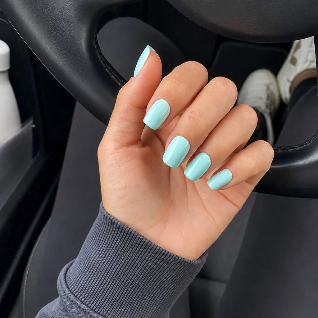 Press-on Nails Vert Lagon carrés courts sur main appuyée sur volant de voiture, pull gris côtelé, faux ongles bleu-vert frais et lumineux LYLY Nails