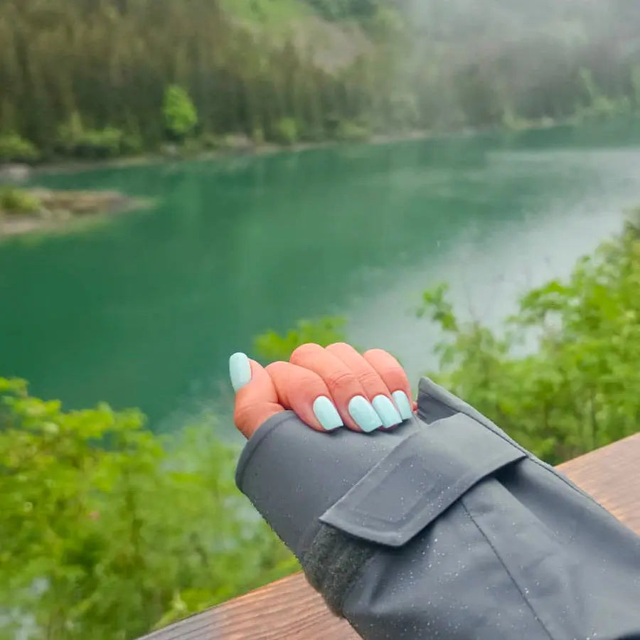 Manucure press-on Vert Lagon carrés courts, main fermée sur rambarde en bois face à un lac de montagne, ambiance randonnée et nature, ongles turquoise vivifiants LYLY Nails